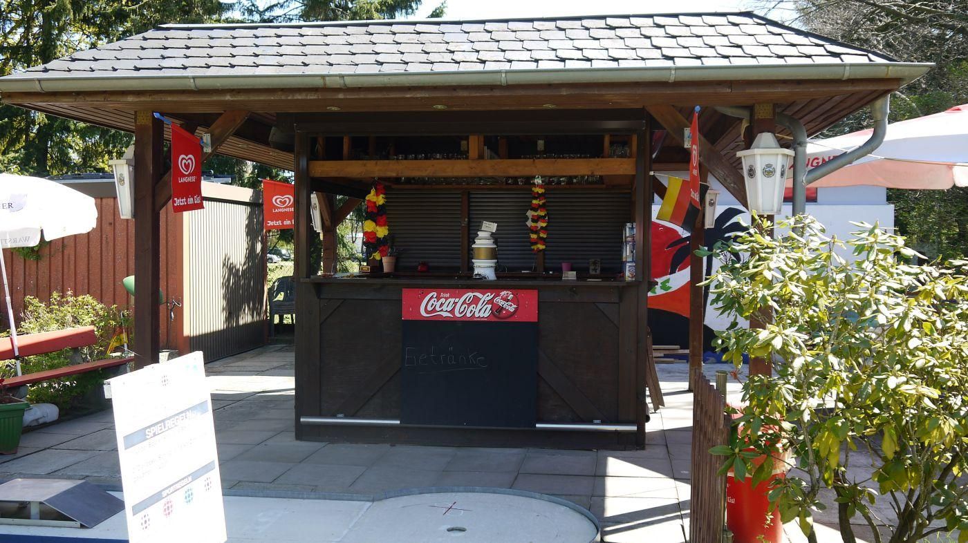 Der Kiosk der Minigolf-Oase mit Holzdach, davor Blumen und ein Werbeaufsteller