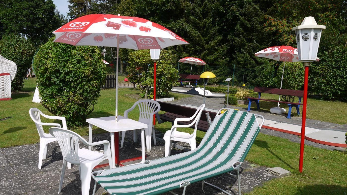 Sitzplätze mit weißen Gartenstühlen und Liegestühlen unter rot-weißen Sonnenschirmen