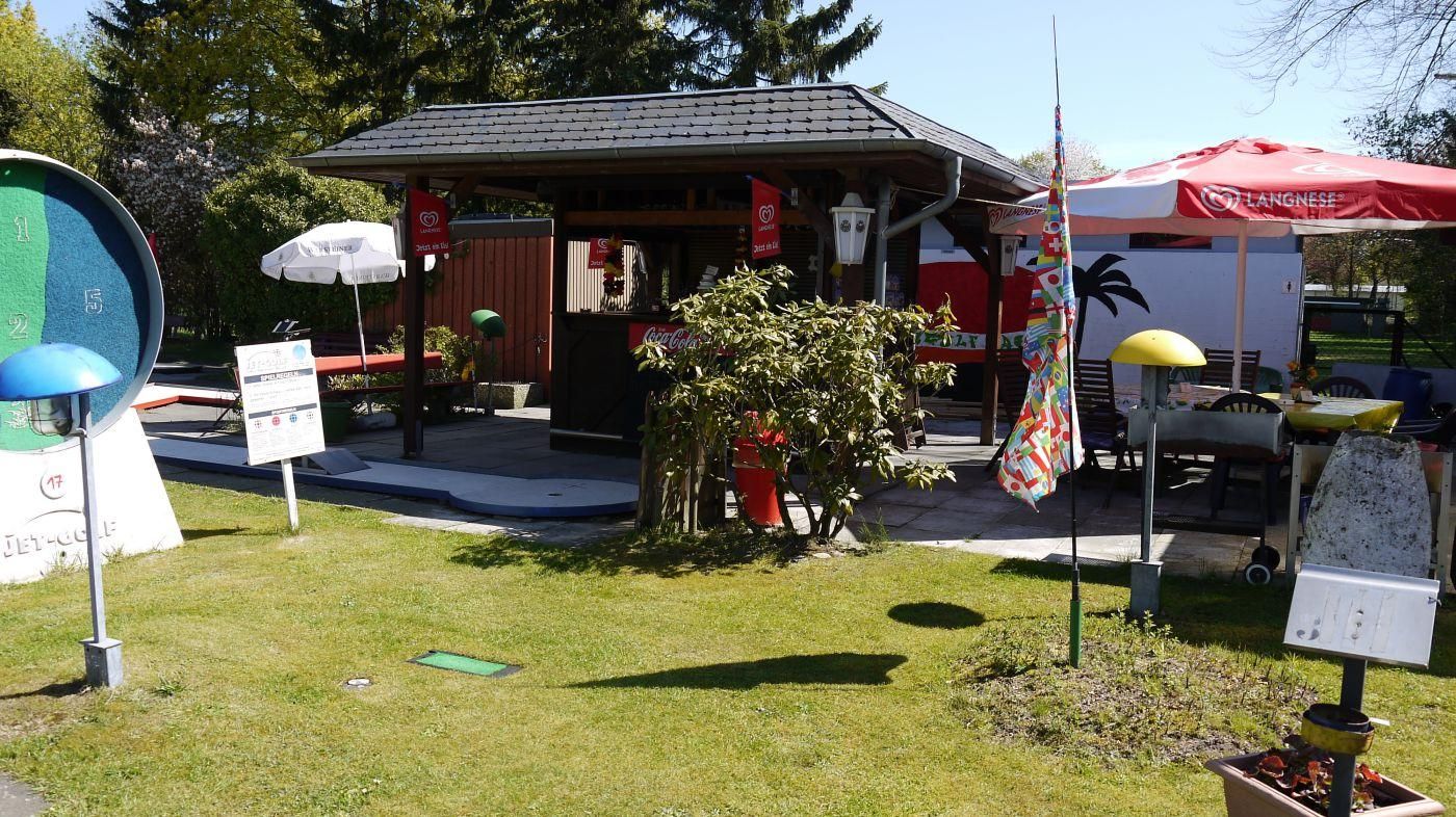 Kiosk der Minigolf-Oase mit Tischen, Sonnenschirmen und Blumen auf der Terrasse
